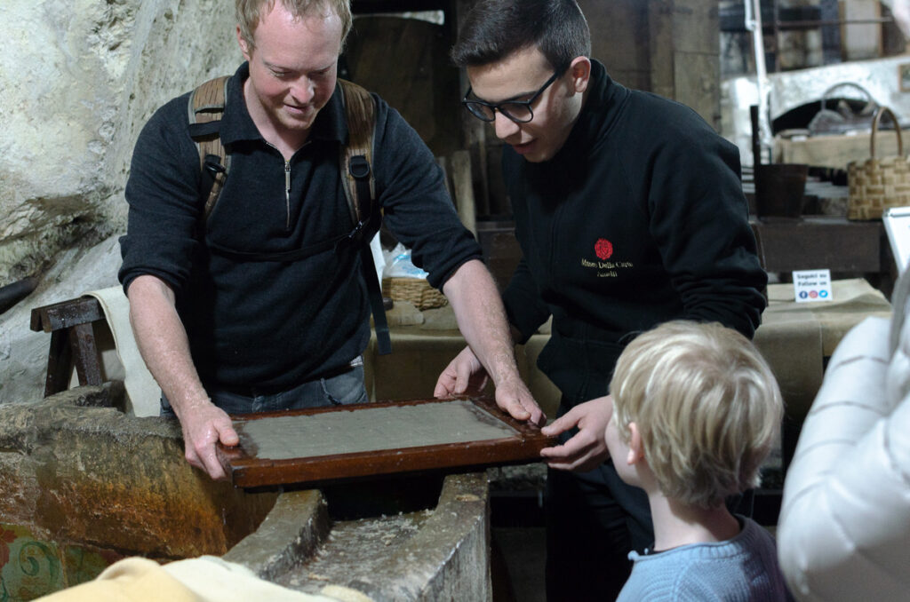 Tourists can make there own paper at the Amalfi Paper Museum with the help of a guide. The visitors are using a wooden frame called "deckle" used in the paper-making process.