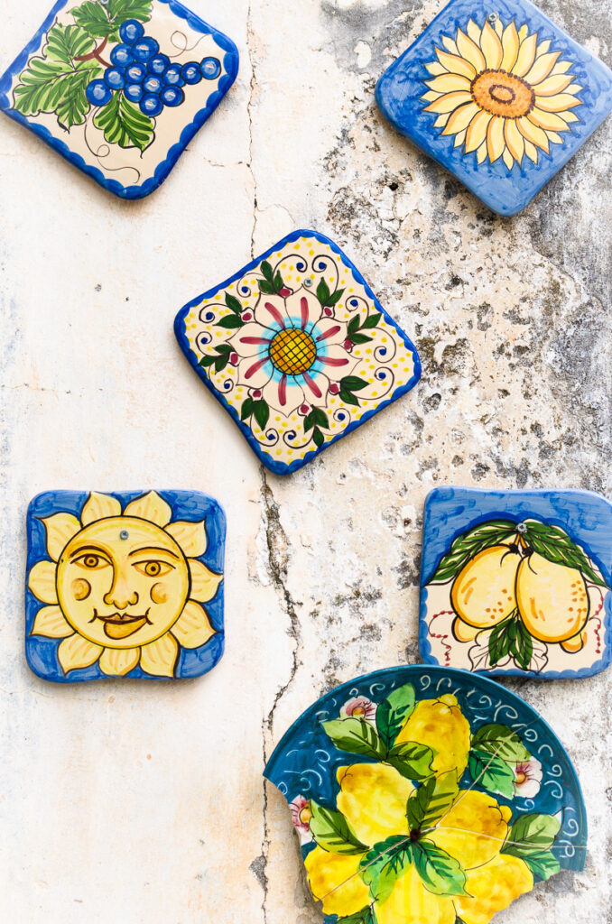 Hand painted Vietri ceramics decorating a wall. the quaint ceramic pieces are hand painted, dominantly blue and yellow. They have sun flowers, lemons and grape painted on them. The ceramics are hanging on a charming old wall