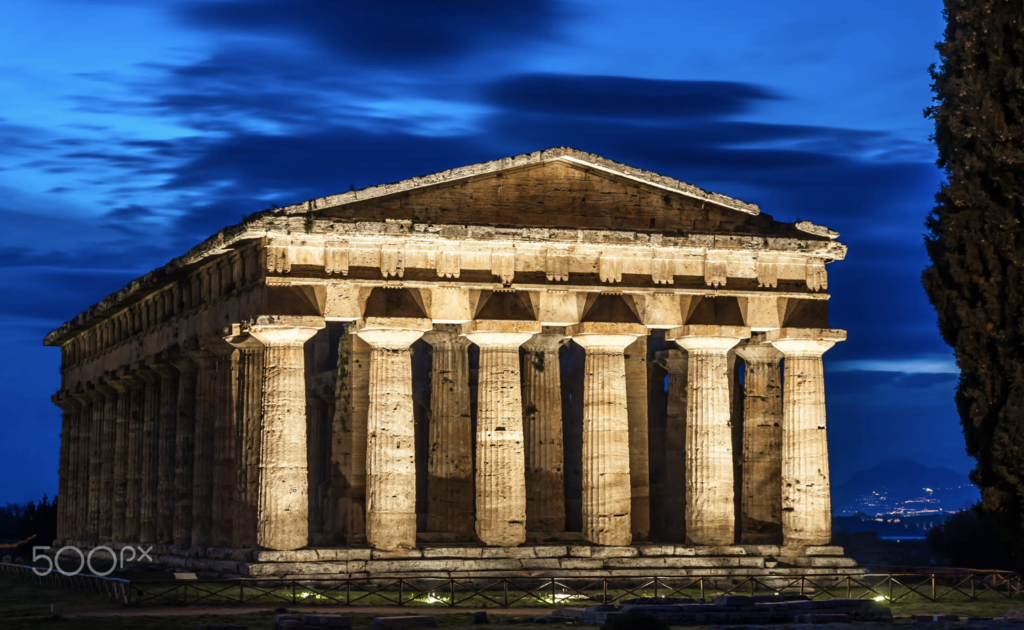The illuminated facade of the greek temple, in the Paestum Archaeological Park in Cilento, Italy. Image taken during blue hour.