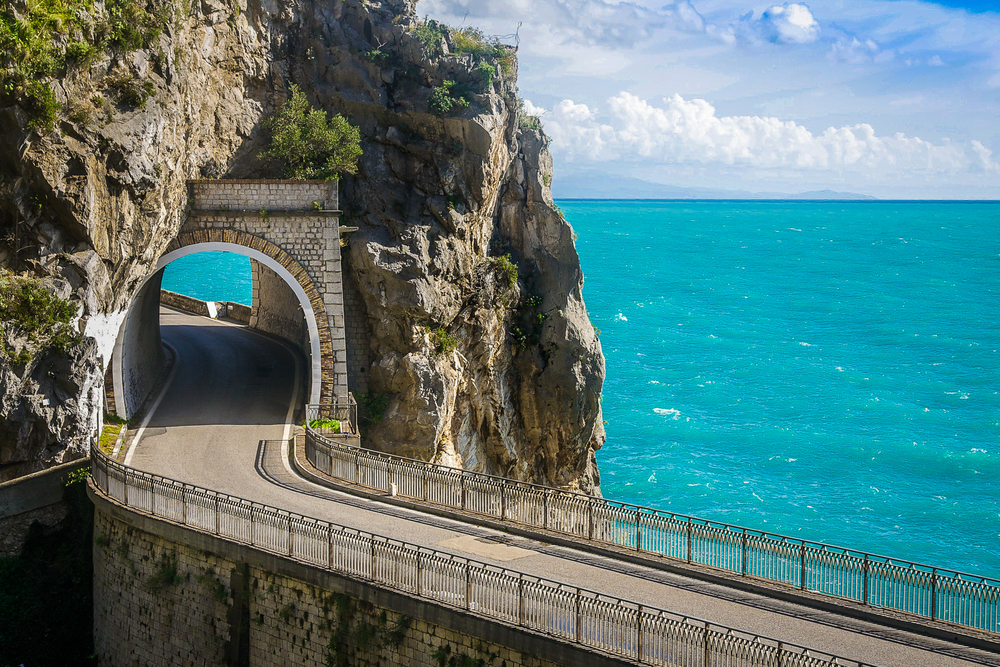 Scenic view of the Amalfi Drive with the turquoise sea in the background and a tunnel through the rocky cliffs.
