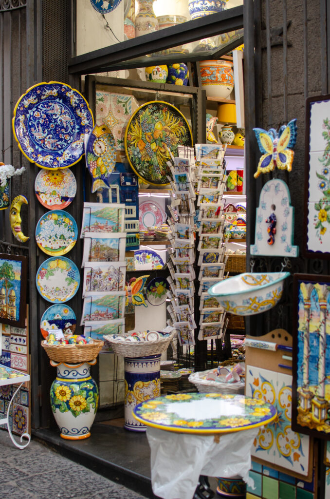 An image of the entrance of a small ceramic shop in Vietri sul Mare. Ceramic pots, plates, postcards and other decorative items can be seen. 