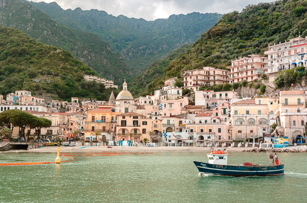The little fishing village of Cetara, as seen from the sea. Fishing boat navigates on the water. Village nestled in a valley under the lush mountains.
