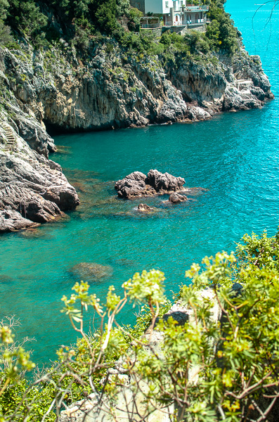 Clearwater Beach, a secluded gem on the Amalfi Coast with turquoise waters. Rocky shore and crystal clear sea water. Greenery on the foreground of image.
