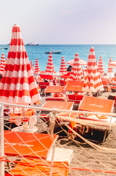The famous beach club Arienzo near Positano. Vibrant orange and white striped umbrellas on the shore.