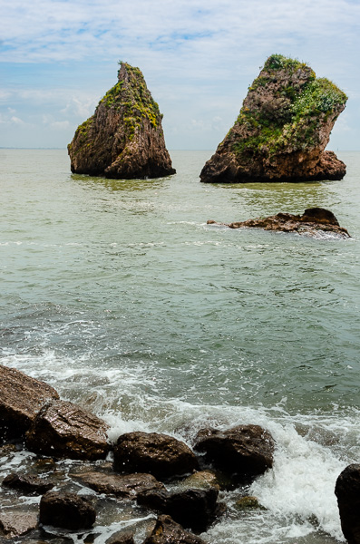 The iconic landmark of Vietri Sul Mare: 'I Due Fratelli,' two striking sea stacks resembling twins. These natural rock formations rise from the sea, mirroring each other's shape. Hence their Italian name is "Fratelli" which means brothers. The two rocks have some green vegetation on their top. 
They are near the shore, at the beach of Vietri Marina.

