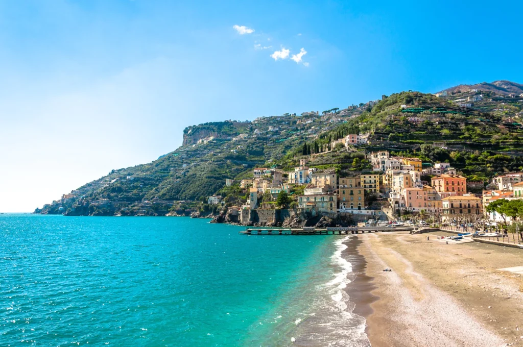 The shore of Minori, and part of the village. The mountains and hills of the Amalfi Coast in the background. Sunny day with turquoise sea water.