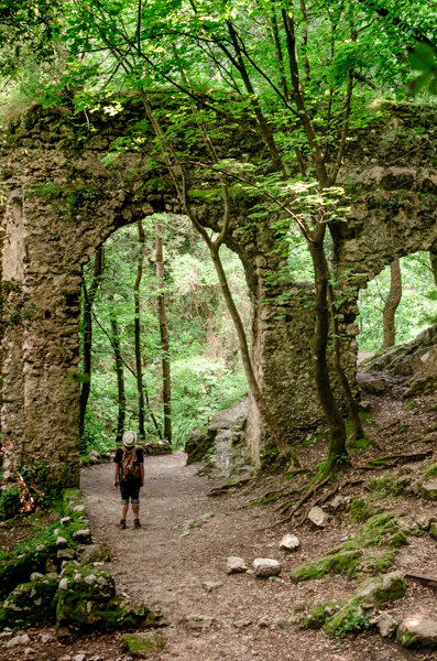 A hiker looks up to the monumental arches over him. The Ruins are on the path of the Valle delle Ferriere, inside the lush green forest.