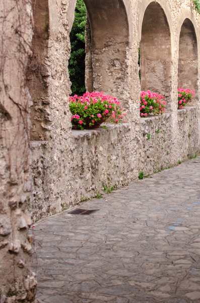 Ancient looking arched stone walls along th small alleyway in Ravello. Pink flowers are growing in each arched opening.
