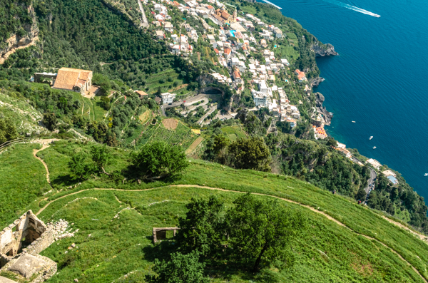 View of the sea and the village of Praiano, from above, and a little pathway across a green meadow. One of the stunning views from the Path of Gods.