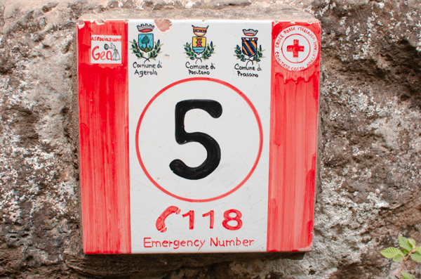 Ceramic signs on a wall, picture taken on the Path of Gods. The hand painted tile has emergency number written on it, and a number 5 to identify your position on the trail in case of need.