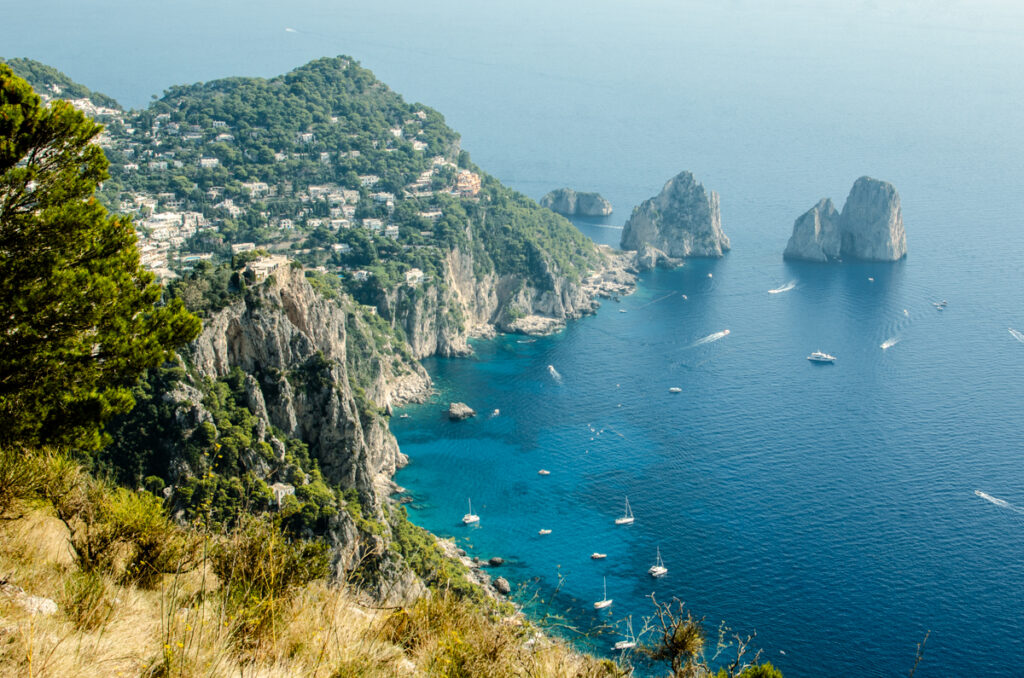 The fantastic view of Capri, from the top of Mount Solaro. High Cliffs, blue sea and the famous Faraglioni rocks. Little sail boats and yacht in the bay.