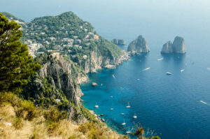 The view of the Faraglioni from the peak of Mount Solaro, in Capri Italy. Azure sea and little boats at the rocky shores of the islands. Mount Solaro is one of the top attraction of ur capri tours.