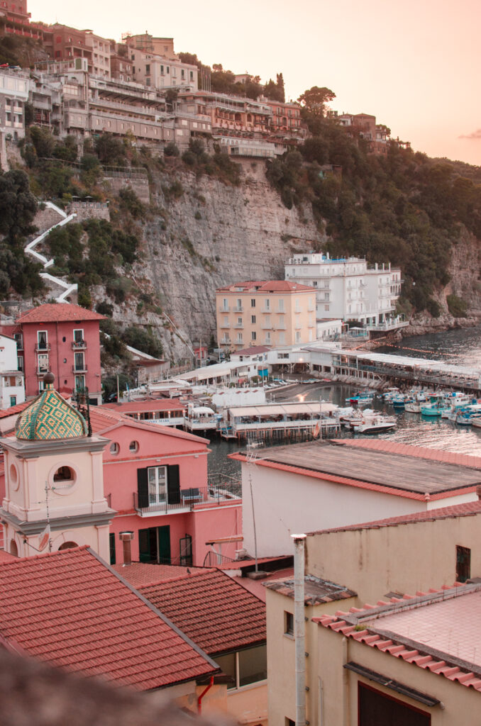 
A glimpse of Marina Grande in Sorrento from above. Pinkish-colored houses, a little bell tower of the church. And a steep cliff in the background, with builddings built over it.