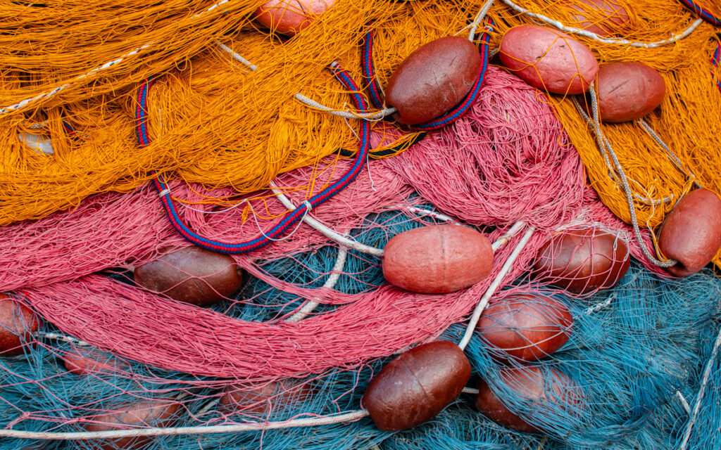 Close-up of a pile of fishing nets with plastic weights, featuring vibrant colors like orange, pink, and blue hues