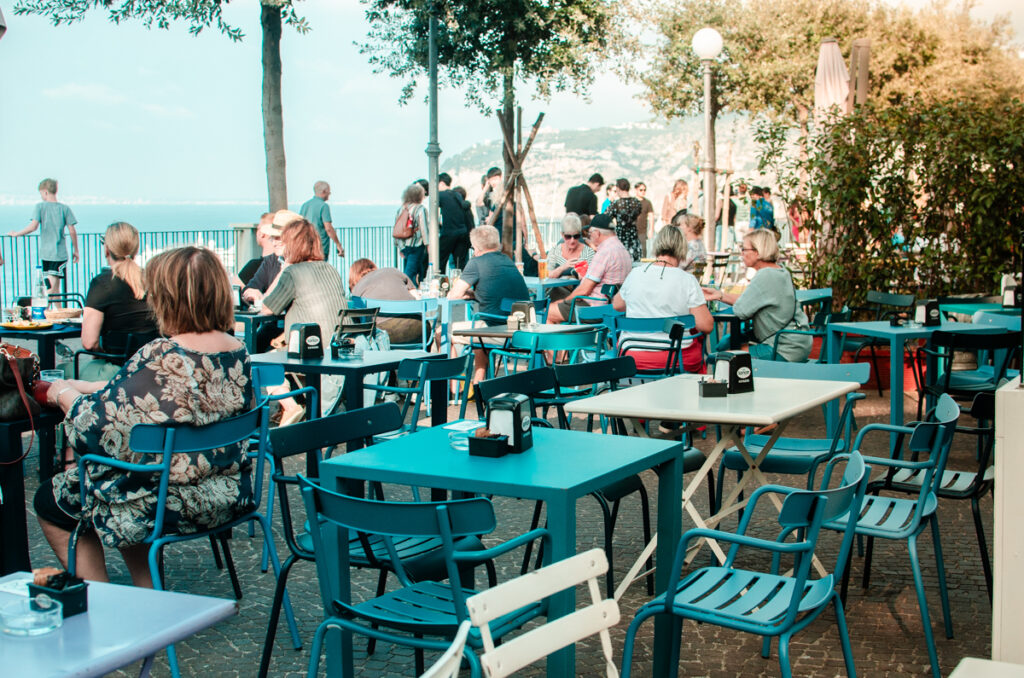 Tables at a caffe near Villa Communale in Sorrento. People In the back walking around and enjoying the view.