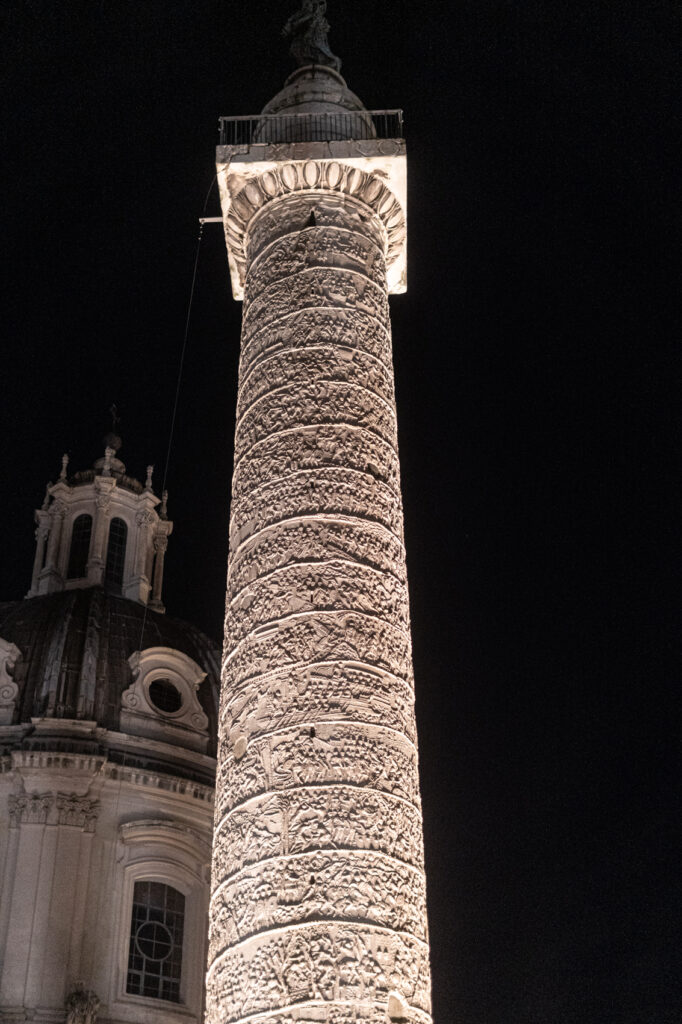 The white marble column of emperor Trajan. Monumental triumphal column with rich reliefs in spiral. Against the night sky.