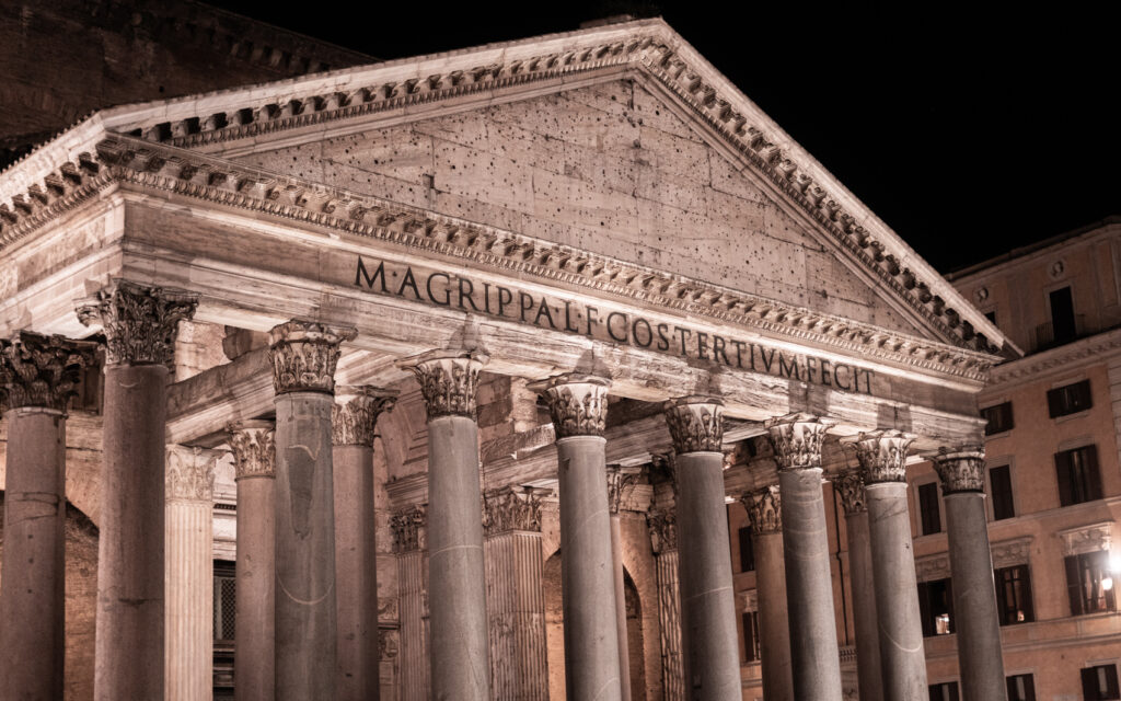 The facade of the Pantheon during our evening walk. Dark, night sky behind the well lit monument.