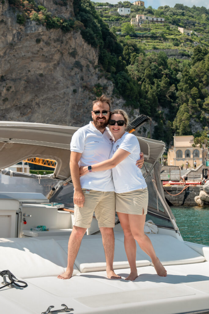 Captain Andrea and his fiancée, the crew of Il Canto del Mare Charter, standing next to each other and smiling at the camera on their boat.